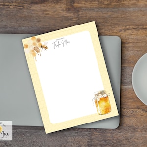 Könnte beinhalten: Ein Briefpapier-Set mit einem Bienen-Thema. Der Notizblock hat einen gelben Bienenwabenrand und Illustrationen von Honig, Bienen und einem Honigglas. Der Notizblock liegt auf einem grauen Laptop mit einer Tasse Kaffee auf einer Holzoberfläche.