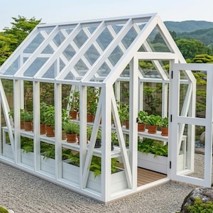 Könnte beinhalten: Ein weiß gerahmtes Gewächshaus mit Glasscheiben und einer offenen Tür. Im Inneren stehen Topfpflanzen auf Regalen. Die Struktur befindet sich in einem Garten mit Kies, Bäumen und einer traditionellen japanischen Ästhetik.