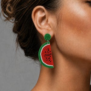 May include: Watermelon slice earrings with green, red, white, and black beads. The earrings have a green circular stud and a beaded watermelon slice design. The earrings are a fun, summery accessory.