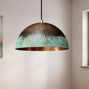 May include: A dome-shaped pendant light fixture featuring a hammered metal texture. The exterior displays a gradient finish transitioning from a dark bronze top to a vibrant turquoise patina base, while the interior reveals a polished copper surface.