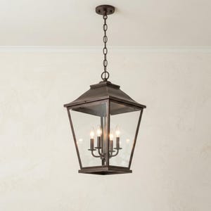 May include: A dark bronze lantern-style pendant light fitting with clear glass panels and a four-light candelabra base. The fitting hangs from a matching metal chain and circular ceiling canopy, featuring a tapered square frame design.
