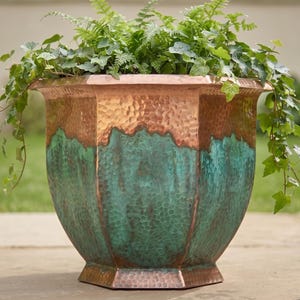May include: A large, octagonal planter featuring a hammered copper finish on the upper rim and base, with a vibrant, weathered teal patina covering the main body. The planter is filled with lush green ivy and fern foliage spilling over the edges.