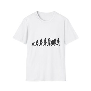 Puede incluir: Una camiseta blanca de manga corta con un estampado gráfico negro en el pecho. El diseño representa la progresión evolutiva de los primates, comenzando con un pequeño simio y terminando con un humano moderno, incluyendo una figura de gorila en el centro.