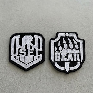 May include: Two black and white embroidered patches. One patch features the word "USEC" with an eagle design. The other patch has the word "BEAR" with bear claw marks. Both patches have a white border.
