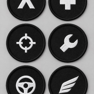 Puede incluir: Un conjunto de seis parches bordados circulares de color negro con iconos blancos. Los diseños incluyen un chevrón hacia arriba, un signo más, una mira, una llave inglesa, un volante y un ala, todos con un borde negro.