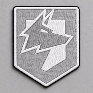 May include: A shield-shaped embroidered patch featuring a stylised wolf head design in shades of light and dark grey. The patch has a thick white border and a thin black outer edge, with a geometric, angular aesthetic throughout the wolf illustration.