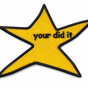 Può includere: Una toppa ricamata a forma di stella con un centro giallo brillante e un bordo nero cucito. Il testo 'your did it' è ricamato con filo nero al centro della stella gialla, caratterizzato da una finitura in tessuto testurizzato.