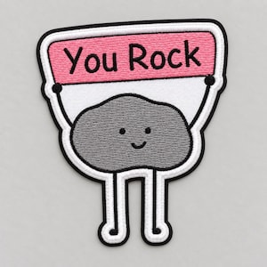 Può includere: Una toppa ricamata raffigurante un personaggio di roccia grigio in stile cartone animato con un volto sorridente e sottili arti bianchi. Il personaggio tiene un cartello rettangolare rosa con il testo nero You Rock, bordato da un bordo nero.