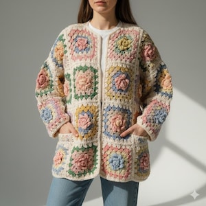 May include: A long-sleeved open-front cardigan constructed from joined crochet granny squares. Each square features a raised floral center in pastel shades of pink, yellow, blue, and green on a cream background. The garment includes two front pockets.