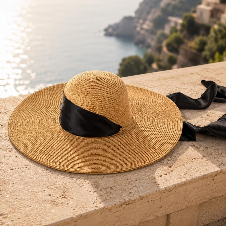 Peut inclure: Un chapeau de paille beige &agrave; larges bords avec un ruban de satin noir. Le chapeau a une couronne arrondie et un large bord circulaire. Le ruban noir est enroul&eacute; autour de la couronne et retombe. Le chapeau est pos&eacute; sur une surface en pierre.