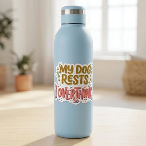 May include: A light blue metal water bottle with a silver cap. A sticker on the front features the text MY DOG RESTS I OVERTHINK in brown and pink lettering, accented with small paw prints and bone shapes on a white background.