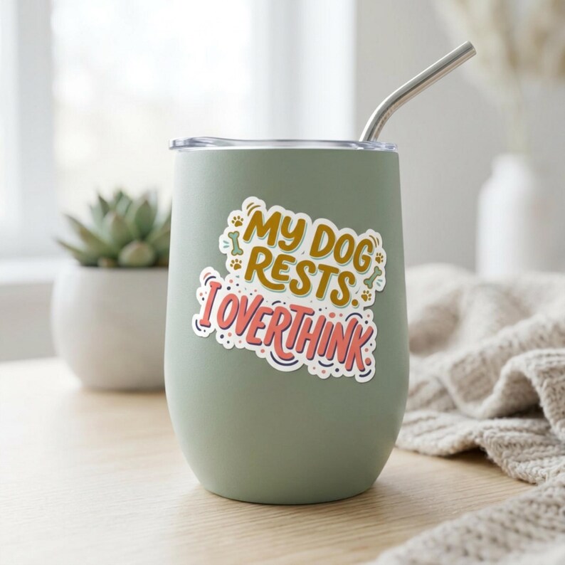 May include: A sage green stainless steel tumbler with a clear lid and a silver metal straw. A sticker on the front features the text "MY DOG RESTS I OVERTHINK" in yellow and pink, surrounded by small decorative paw prints and bone icons.