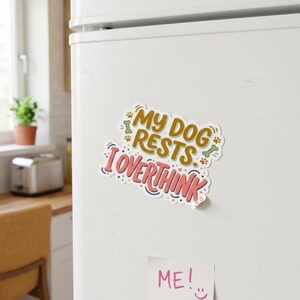May include: A rectangular magnet with rounded edges featuring the text MY DOG RESTS I OVERTHINK in gold and pink lettering. The design includes small green bone icons and brown paw prints, all set against a white background on a refrigerator.