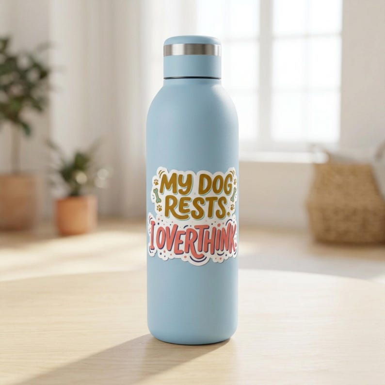 May include: A light blue metal water bottle with a silver cap. A sticker on the front features the text MY DOG RESTS I OVERTHINK in brown and pink lettering, accented with small paw prints and bone shapes on a white background.