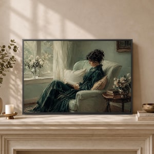 May include: A framed wall art print depicting a person with dark hair styled in an updo, wearing a long dark green dress, sitting in a light-colored armchair by a window while reading a book. A small wooden side table with flowers sits nearby.