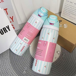May include: Two insulated water bottles with a light blue and white striped pattern and small cherry illustrations. Each bottle has a pink label and a light blue lid. The bottles are designed to keep drinks cold for 24 hours.