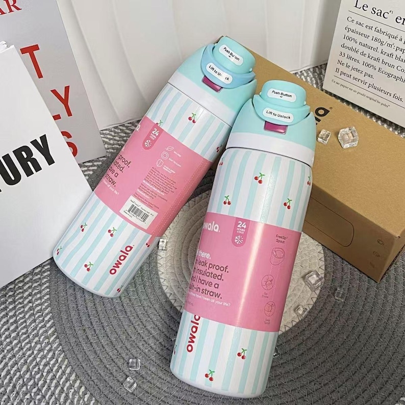 May include: Two insulated water bottles with a light blue and white striped pattern and small cherry illustrations. Each bottle has a pink label and a light blue lid. The bottles are designed to keep drinks cold for 24 hours.