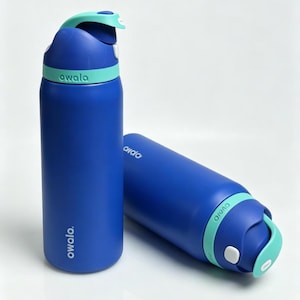 May include: Two blue Owala water bottles with teal accents. One bottle is upright, the other is lying down. The bottles have a flip-top lid with a handle and the brand name printed on the side. The bottles are designed for hydration.