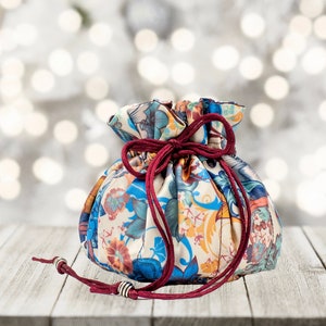 May include: A colorful drawstring bag with a floral pattern and red cord. The bag is sitting on a wooden surface.
