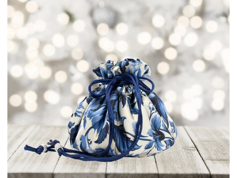 May include: A blue and white floral drawstring bag with a navy blue cord. The bag is sitting on a wooden surface.