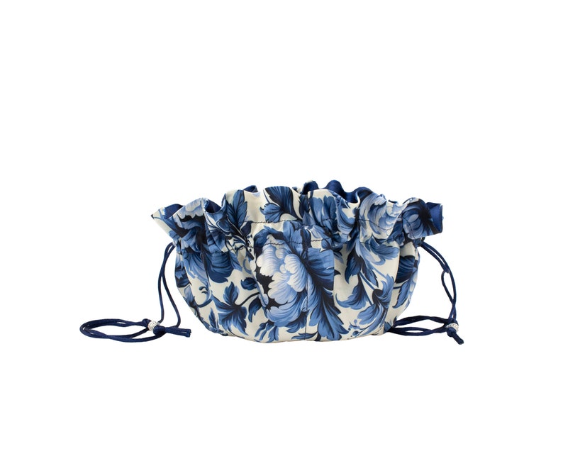 May include: A blue and white floral drawstring pouch with a ruffled top and blue drawstrings.