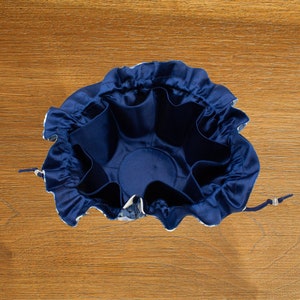 May include: A blue drawstring bag with a ruffled top and multiple compartments inside. The bag is made of a soft, silky fabric.