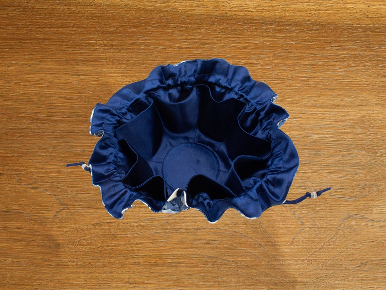May include: A blue drawstring bag with a ruffled top and multiple compartments inside. The bag is made of a soft, silky fabric.