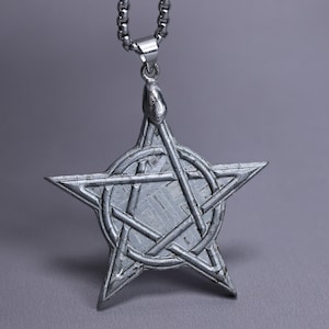 Puede incluir: Un colgante de metal plateado con forma de estrella de cinco puntas y un intrincado patrón de líneas geométricas superpuestas grabado en la superficie. El colgante cuelga de una cadena de metal plateado a juego con un acabado metálico pulido.