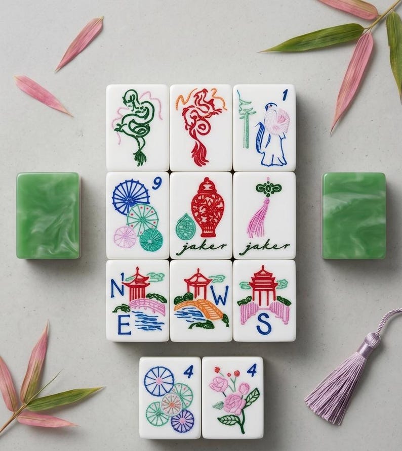 May include: A set of white Mahjong tiles featuring colorful illustrations of dragons, floral patterns, a red vase, and pagodas. Some tiles display the letters N, E, W, S and the word jaker. Two solid green marbled tiles are placed on the sides.