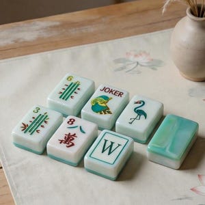 May include: A set of seven rectangular mahjong tiles with a pale green and white marbled finish. The tiles feature various designs including green bamboo stalks, a red Chinese character, a Joker label, a green crane, and a letter W.