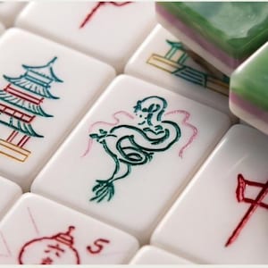 May include: A collection of white rectangular mahjong tiles featuring engraved and painted designs in red, green, and blue. The tiles display various symbols including a pagoda, a dragon, and Chinese characters, with some stacked green tiles.