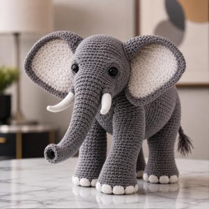 May include: A crocheted gray elephant with large, white-lined ears, white tusks, and black eyes. The handmade elephant has a long trunk and a small tail. The feet are detailed with white accents. This soft sculpture is a decorative item.