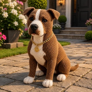 May include: A brown and white crocheted dog figurine sitting in a fixed position. The dog features a white stripe running from its forehead to its chest and white paws. It wears a gold-colored chain necklace with a round pendant showing a paw print.