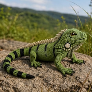 Op de afbeelding: Een handgemaakte gehaakte leguaan in groen-, zwart- en bruintinten, geposeerd op een rots. Het reptiel heeft gedetailleerde steken, zwarte strepen en een getextureerde ruggengraat. Het oog van de leguaan is warmbruin.