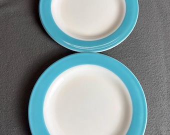 May include: Two round ceramic plates featuring a smooth white center and a wide, solid turquoise blue rim. The plates are arranged vertically, one above the other, showcasing a clean, simple design with a glossy finish on the surface.