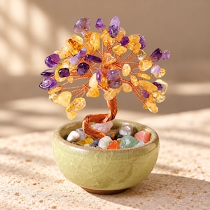 Puede incluir: Una escultura de árbol decorativa con ramas de alambre de cobre trenzado adornadas con fragmentos de piedras preciosas de amatista morada y citrino amarillo. El árbol está colocado en un pequeño cuenco de cerámica verde claro con piedras.