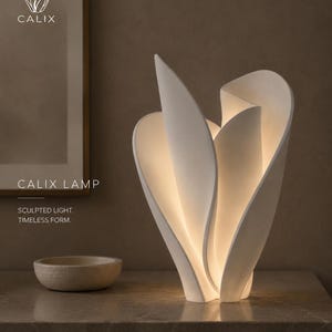 Peut inclure: Une lampe Calix blanche avec une forme sculpturale rappelant des pétales, émettant une douce lueur interne. Le texte CALIX, CALIX LAMP, SCULPTED LIGHT et TIMELESS FORM est visible. Un petit bol beige rond est posé à gauche de la lampe.