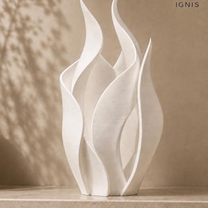 Op de afbeelding: Een witte sculpturale vaas met een vlamachtig, gelaagd ontwerp met gebogen, verticale panelen. Het object heeft een matte textuur en bevat een klein logo in de rechterbovenhoek met een vlamicoon en de tekst IGNIS eronder gedrukt.