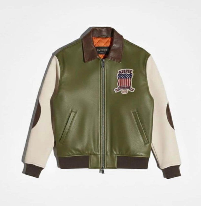 May include: Olive green leather jacket with cream-colored sleeves and brown accents. Features a brown collar, a zip-up front, and a patch on the chest with the text "AVIREX". The jacket has a ribbed hem and cuffs.