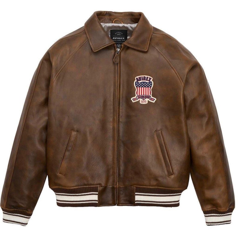 Puede incluir: Chaqueta de cuero marr&oacute;n con cremallera, cuello y pu&ntilde;os y dobladillo acanalados. Presenta un parche con un dise&ntilde;o de bandera americana y la marca "AVIREX". La chaqueta tiene dos bolsillos delanteros y un estilo bomber cl&aacute;sico.