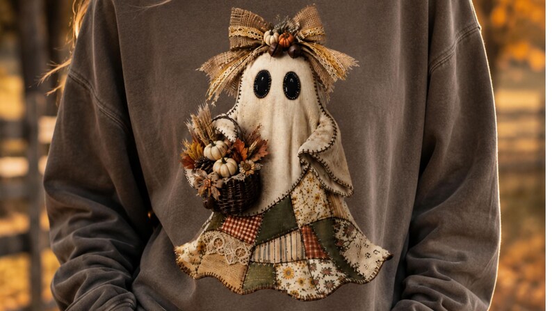 May include: A charcoal grey sweatshirt featuring a central graphic of a ghost figure. The ghost has black oval eyes, a hessian bow on its head, and holds a dark wicker basket filled with miniature pumpkins, wheat, and autumn leaves.