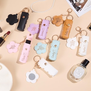 Può includere: Una collezione di custodie rettangolari per rossetto con chiusure a scatto dorate e ciondoli a forma di fiore. Ogni custodia presenta un nome personalizzato e un'incisione floreale. Le custodie sono disponibili in nero, lavanda, marrone chiaro, rosa, azzurro e bianco.
