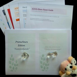May include: A collection of printed documents, including a guide titled "ADHS-Eltern Reset-Guide." The documents are stacked, with the top one featuring text and a pink header. The image also shows a clear, faceted crystal and a plush toy.