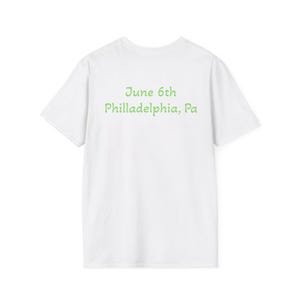 May include: White t-shirt with green text that reads "June 6th Philadelphia, Pa." The shirt is plain on the front and has a crew neck. The text is centered on the back of the shirt.