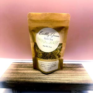 Puede incluir: Una bolsa de papel kraft marrón que contiene té de baño Earthly Green con un peso neto de 2 oz. La etiqueta muestra el nombre del producto y una lista de ingredientes que incluye raíz de jengibre seca, cúrcuma, limoncillo y aceite esencial de jengibre.