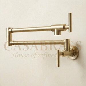 May include: A wall-mounted pot filler faucet with a brushed brass finish, featuring a double-jointed articulating arm, two vertical lever handles, and a circular wall plate. The text CASABRASS House of refined is visible across the center.