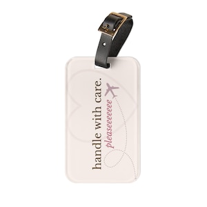 May include: A rectangular luggage tag with a cream background and a black leather strap. The tag has the text "handle with care. Pleaseeeeeee" and a purple airplane graphic.