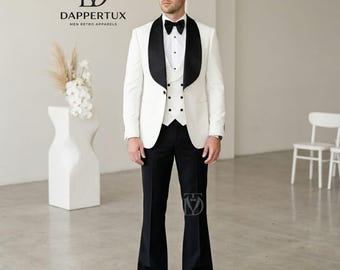 May include: A white tuxedo jacket with black shawl lapels, a white button-down shirt, a black bow tie, a white double-breasted vest with black buttons, and black flared trousers. The Dappertux logo and text are visible in the upper left corner.