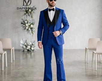 May include: A vibrant royal blue suit featuring a tailored jacket with black peak lapels, a matching vest, and flared trousers. The ensemble includes a crisp white dress shirt, a black bow tie, and black dress shoes, accented by dark sunglasses.