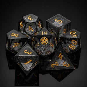 May include: Set of seven polyhedral dice. Each die is black with gold numbering and a glittery interior. The D20 die features a gold pentagram. The dice are displayed on a reflective black surface.